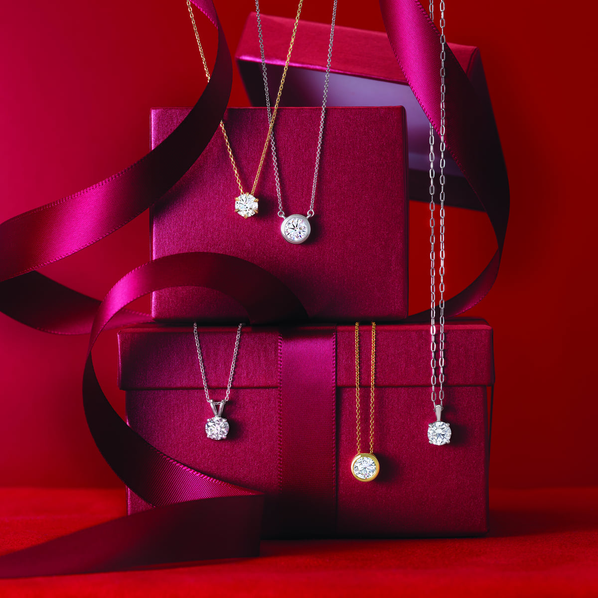 Diamond pendant necklaces draped over red gift boxes with satin ribbon