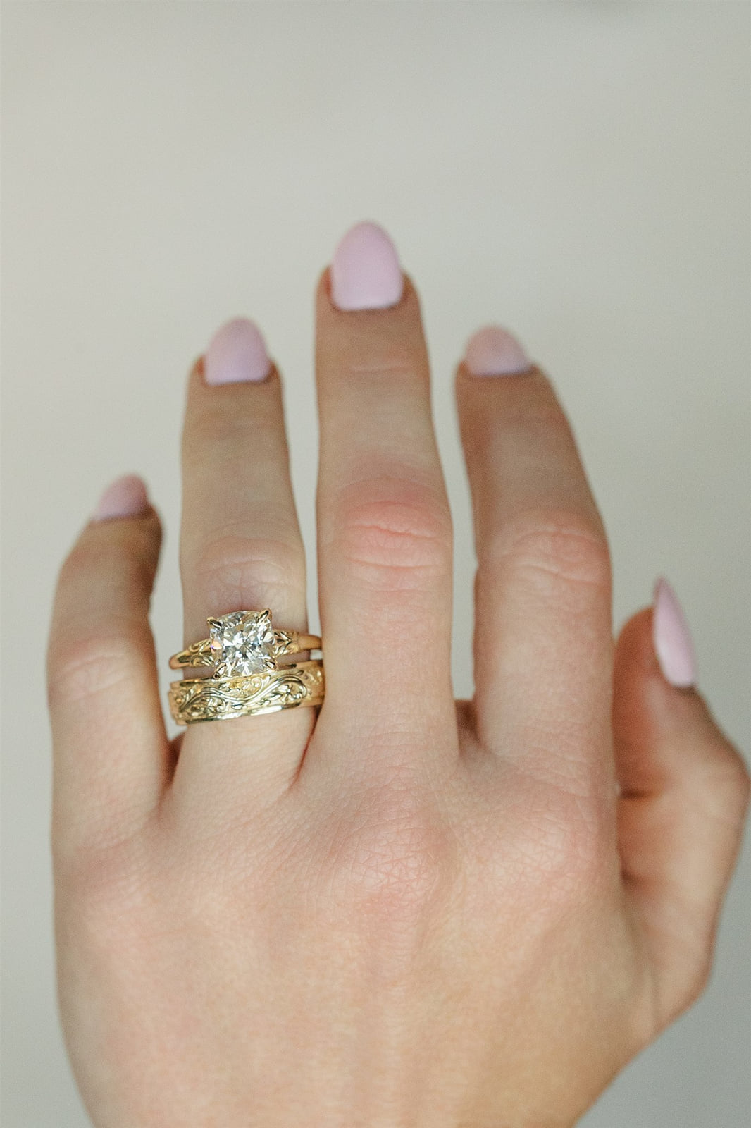 A cushion-cut diamond engagement ring stacked with an engraved yellow gold band